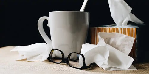 A cup of coffee sits on a table with a box of tissues and a pair of glasses.