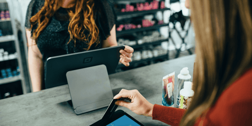 Two people are in frame. One person is cashing out the other at the cash register.