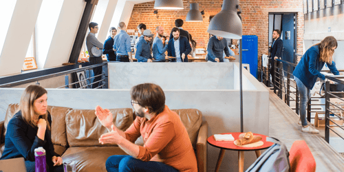 Several people talk with one another in various parts of a lively office building. 