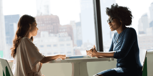 Two people sit across from one another having an interview style conversation. 