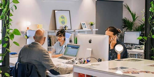 Three people sit working at their desks in a work pod.
