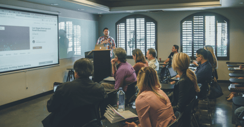 A group sits in a room attending a seminar with the lecturer at the front of the room.