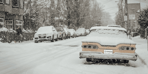 Parked cars in a busy street during a snowstorm.
