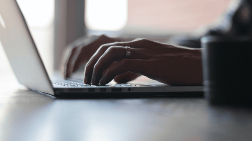 A person sits typing on their computer in a darkly lit room