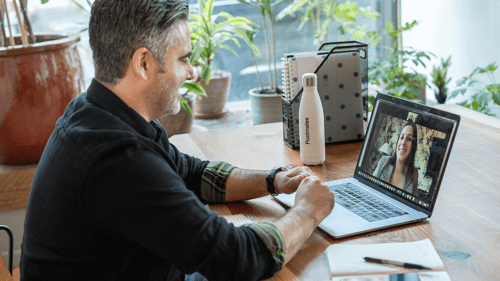 One person sits at their desk on their laptop engaging in a video call with someone else on the screen.