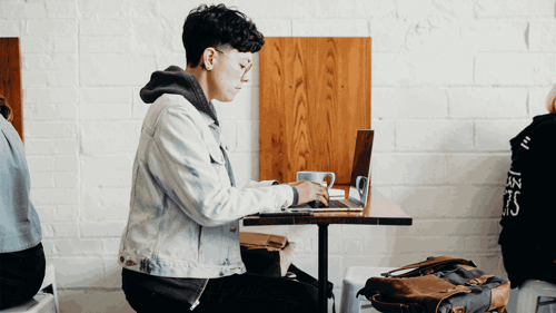 A person sits in a cafe working on their laptop at a table by themselves. 