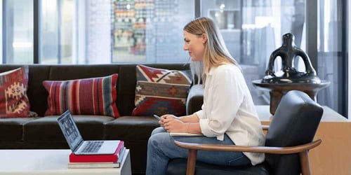 The side profile of someone sitting on a chair talking to their laptop that is rested on their table.