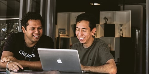 Two coworkers sit together reviewing the contents of a computer screen.