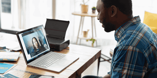 A person sitting at their desk looks at their laptop screen engaging with someone on a video call.