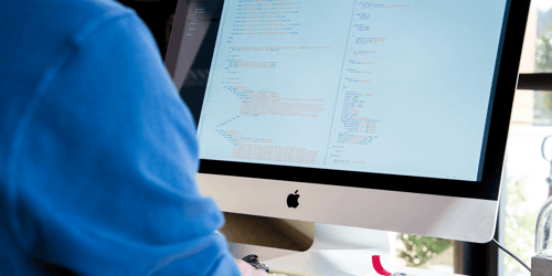 A person sits looking at their computer with the coding work they're doing viewable on screen.