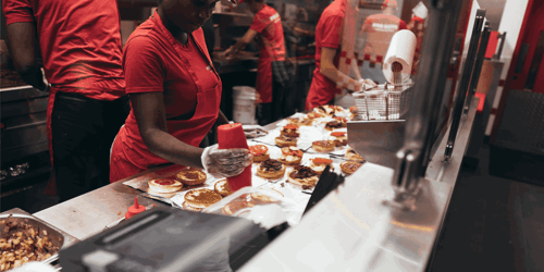 Several employees work in a kitchen assembling quick service food.