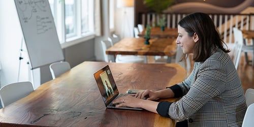 A person sits in an open concept office on a video call.