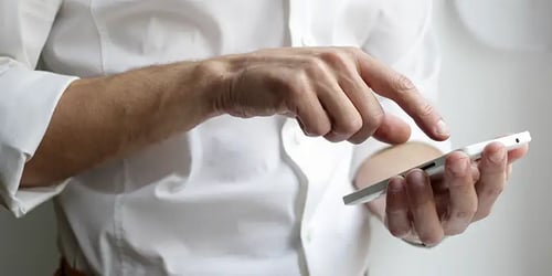 Someone in a white button down with only their hands and torso in view scrolling on their phone. 