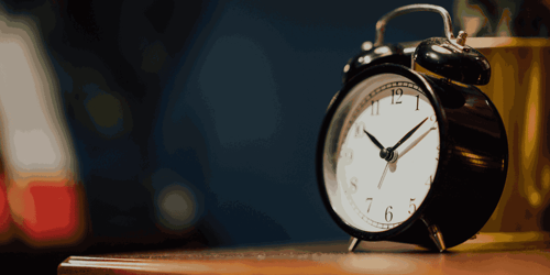 A black clock sits on top of a wooden table.