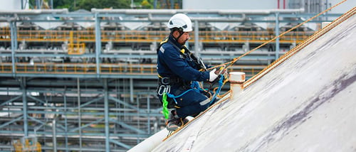 Construction worker on roof wearing white helmet and blue body suit