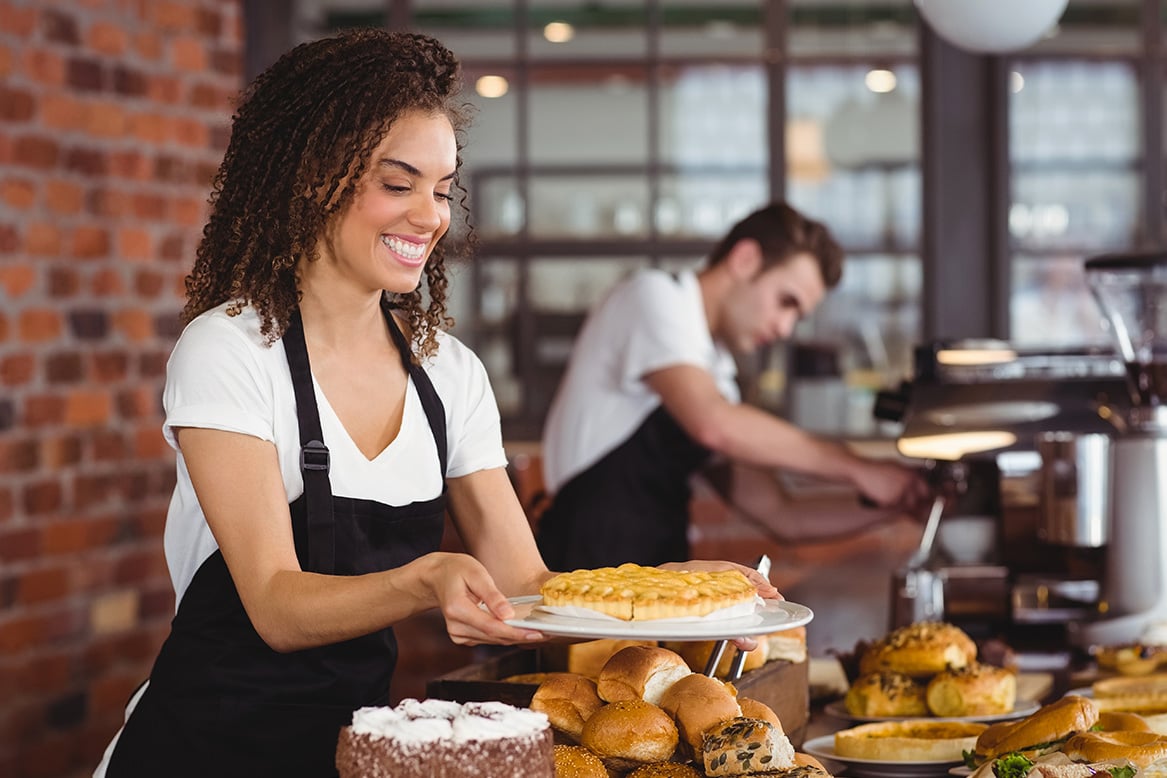 Smiling waitress holding cake in front of colleague