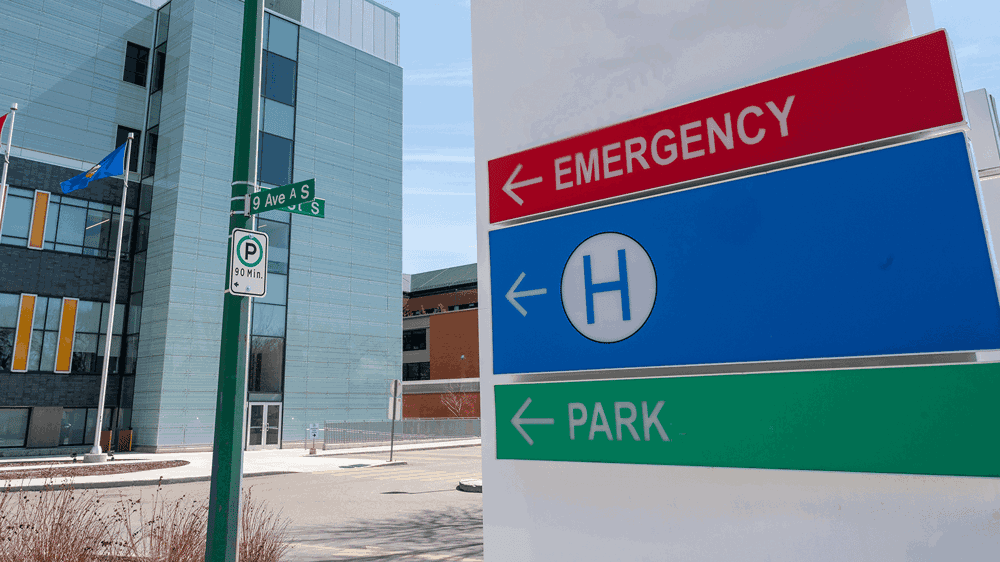 A sign on a street corner indicating where the hospital is and it's emergency entrance.