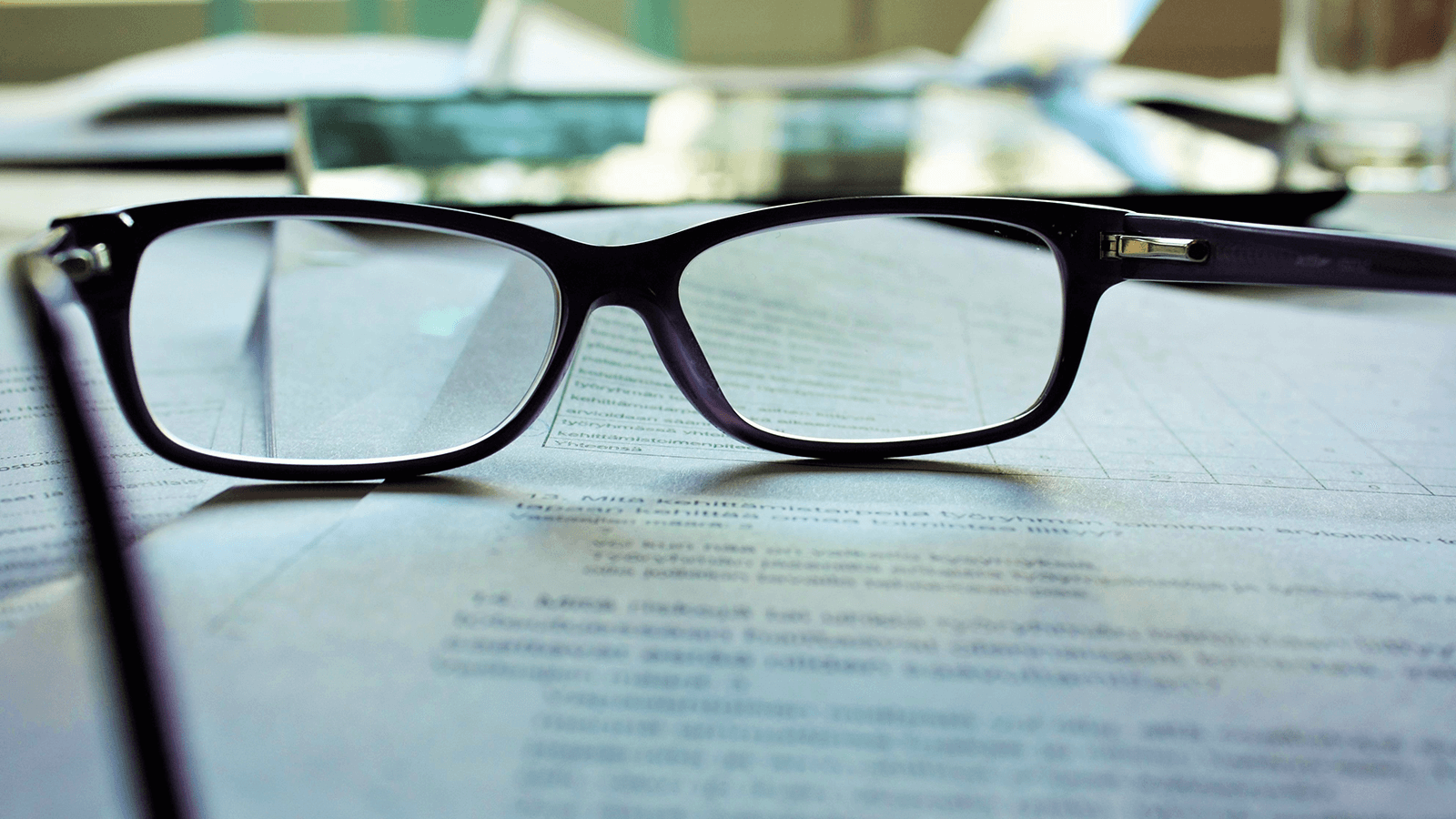 A pair of glasses rests on top of a stack of paperwork