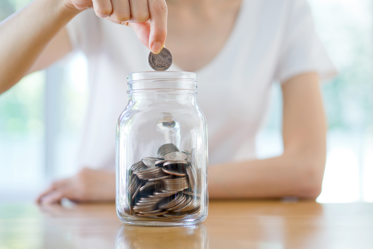 A person is dropping a quarter into a mason jar filled with coins