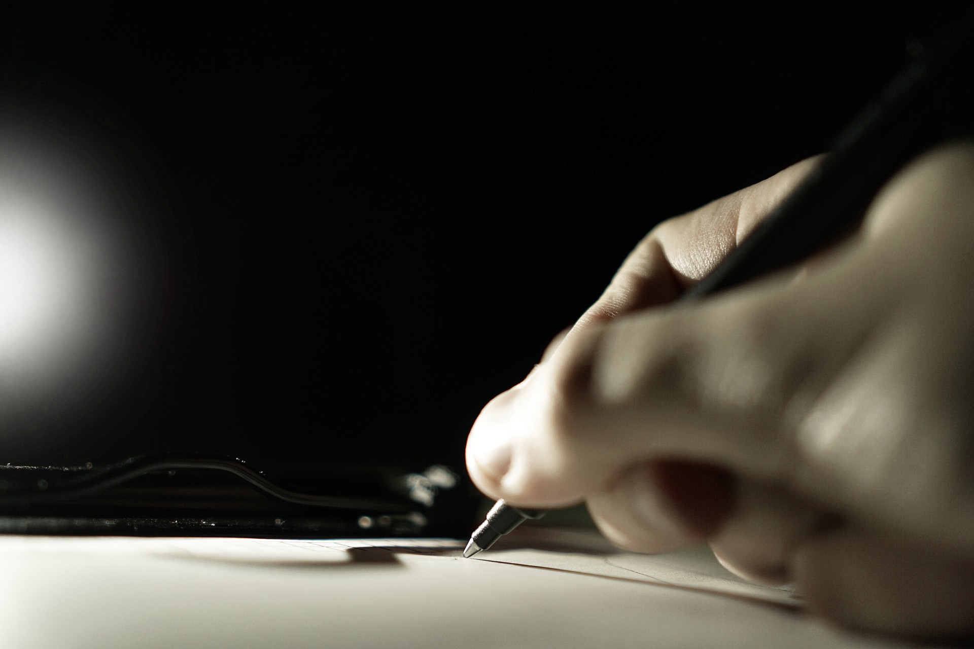 A hand is writing on an illuminated piece of paper