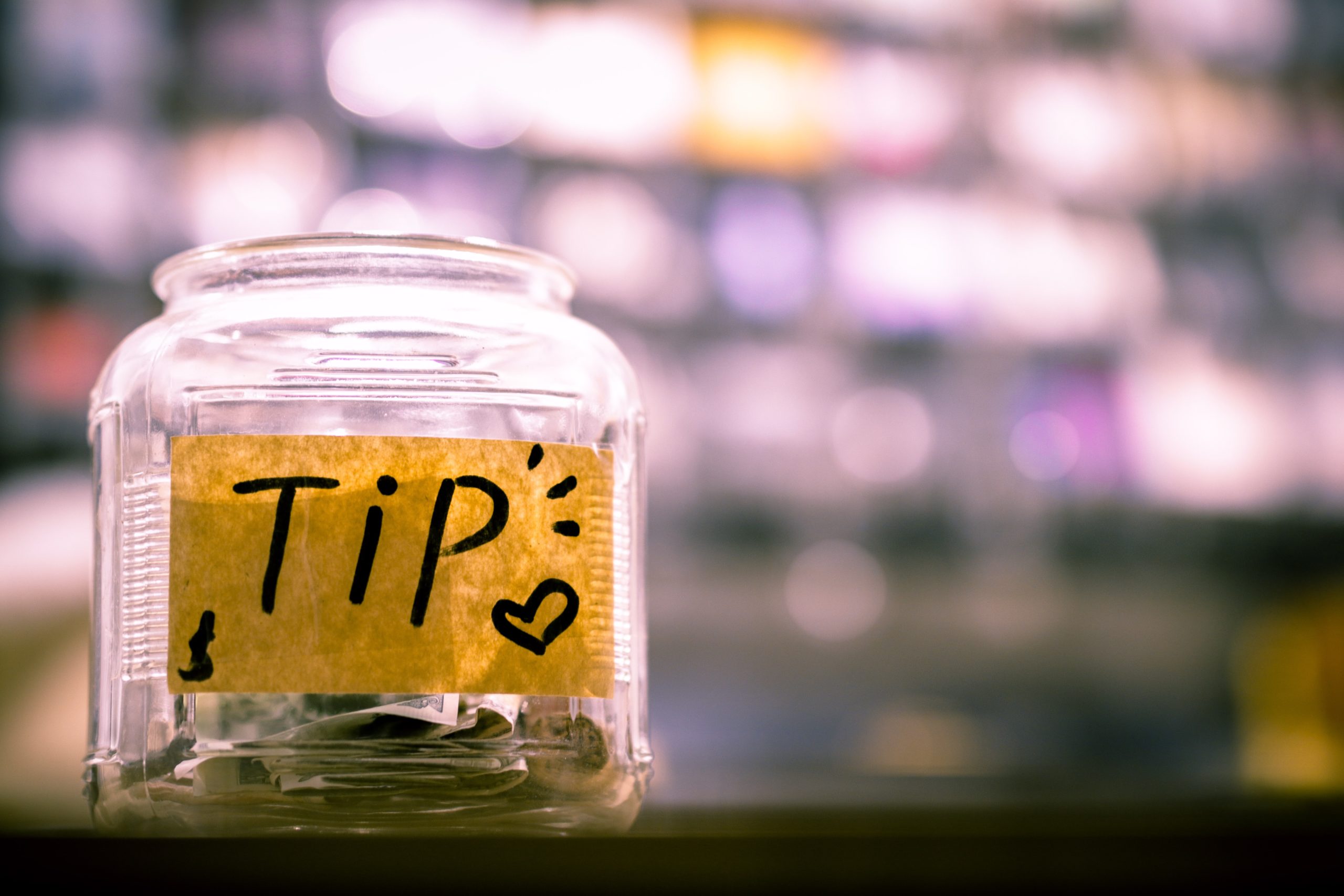 A tip jar sits on the counter of an illuminated bar