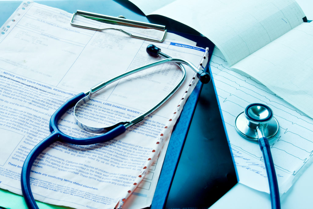 A stethoscope sits on a table on top of a clipboard with paperwork 