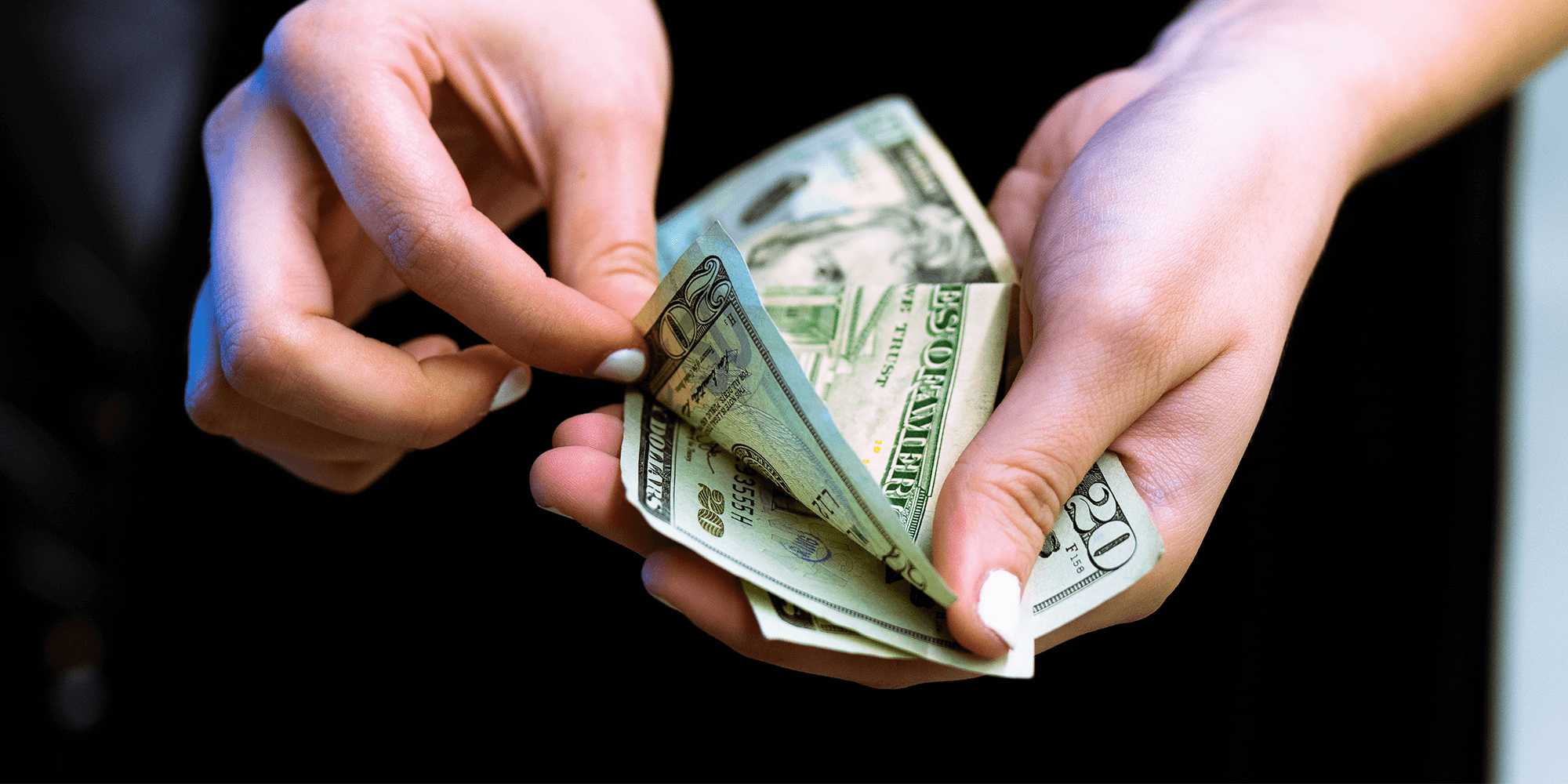 A person with their finger nails painted holds money in their hand counting it.