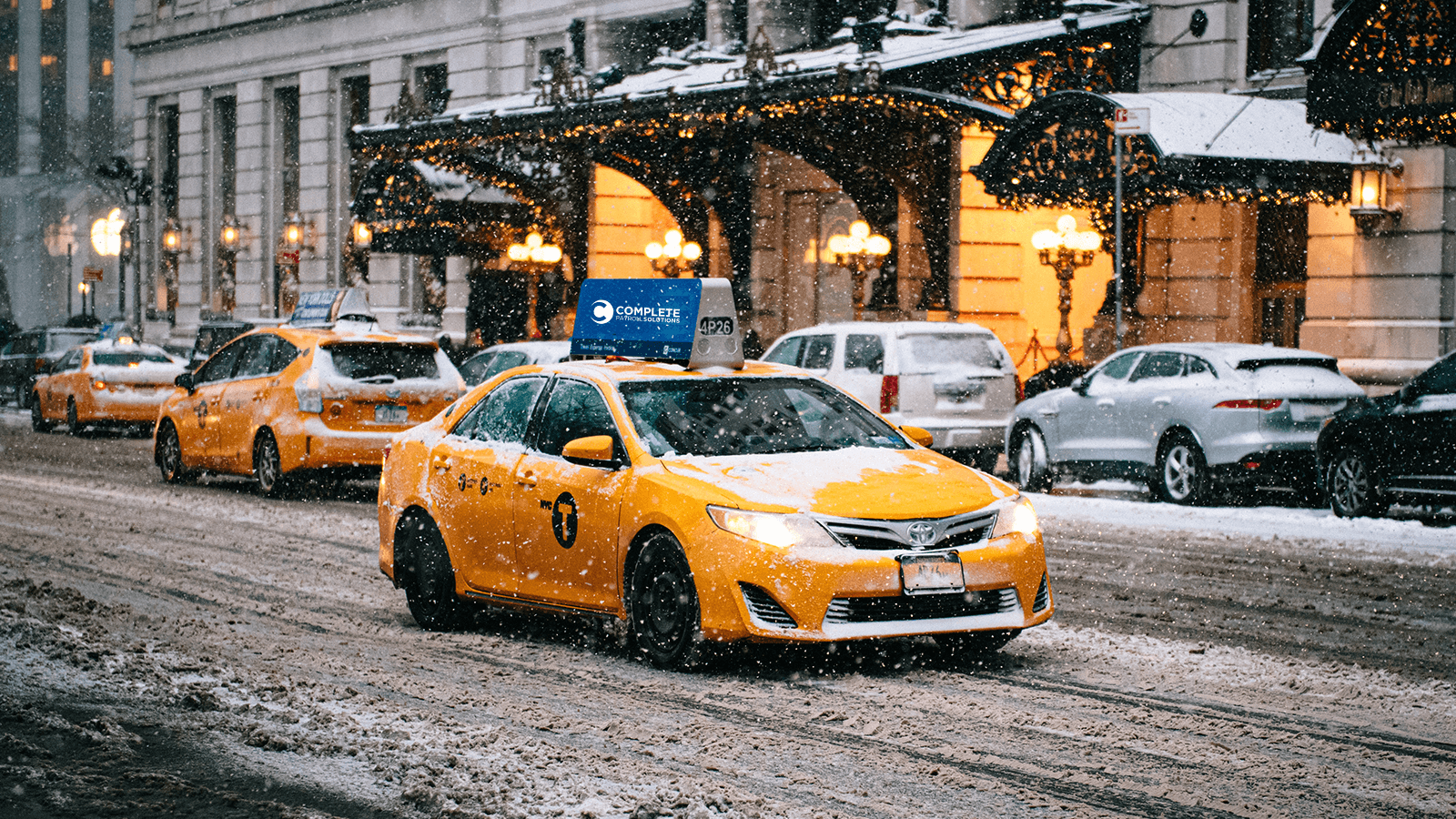 A yellow cab drives through a snow covered road in a city